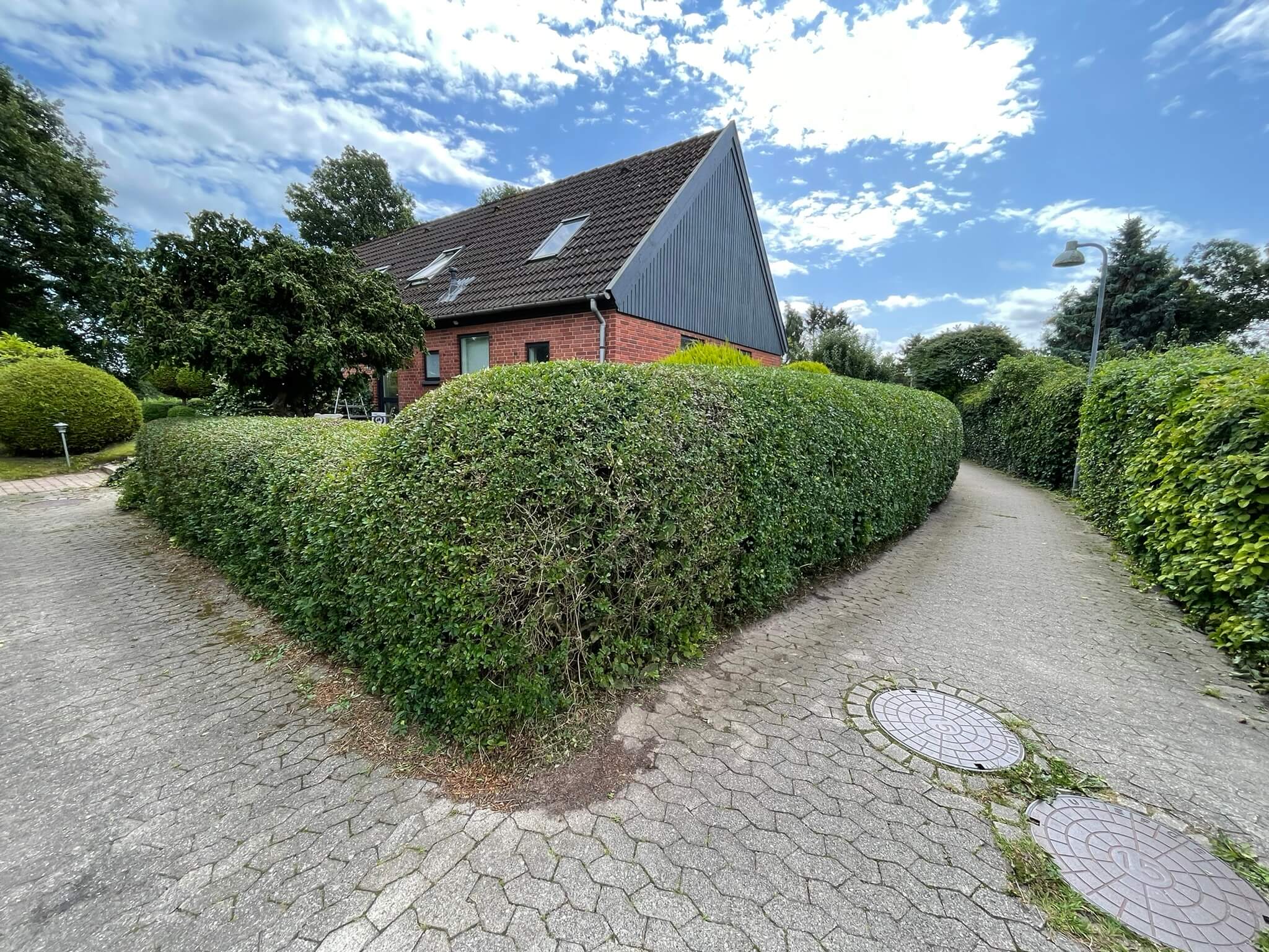 Klippet hæk ved indkørslen til et rødt murstenshus