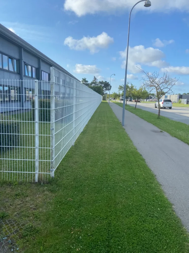 Nyslået græsrabat langs hegn ved erhvervsområde