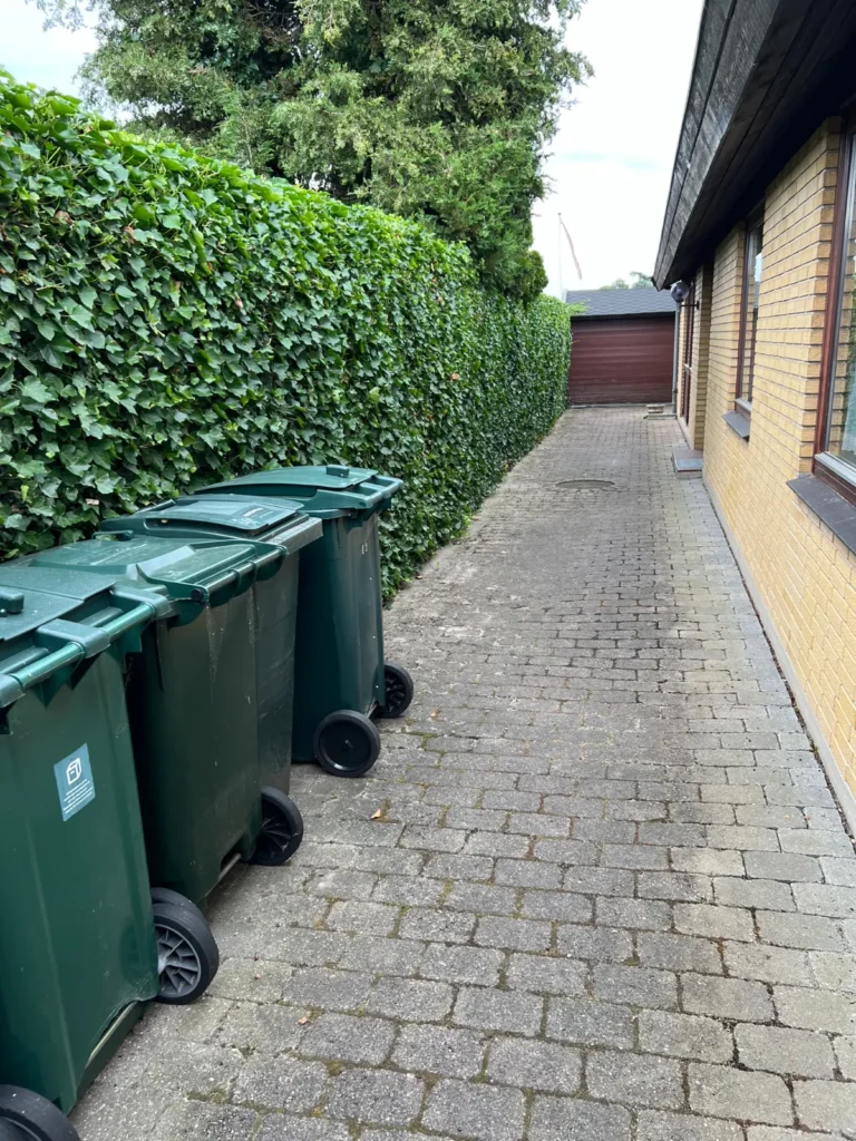 Klippet hæk ved indkørsel med skraldespande