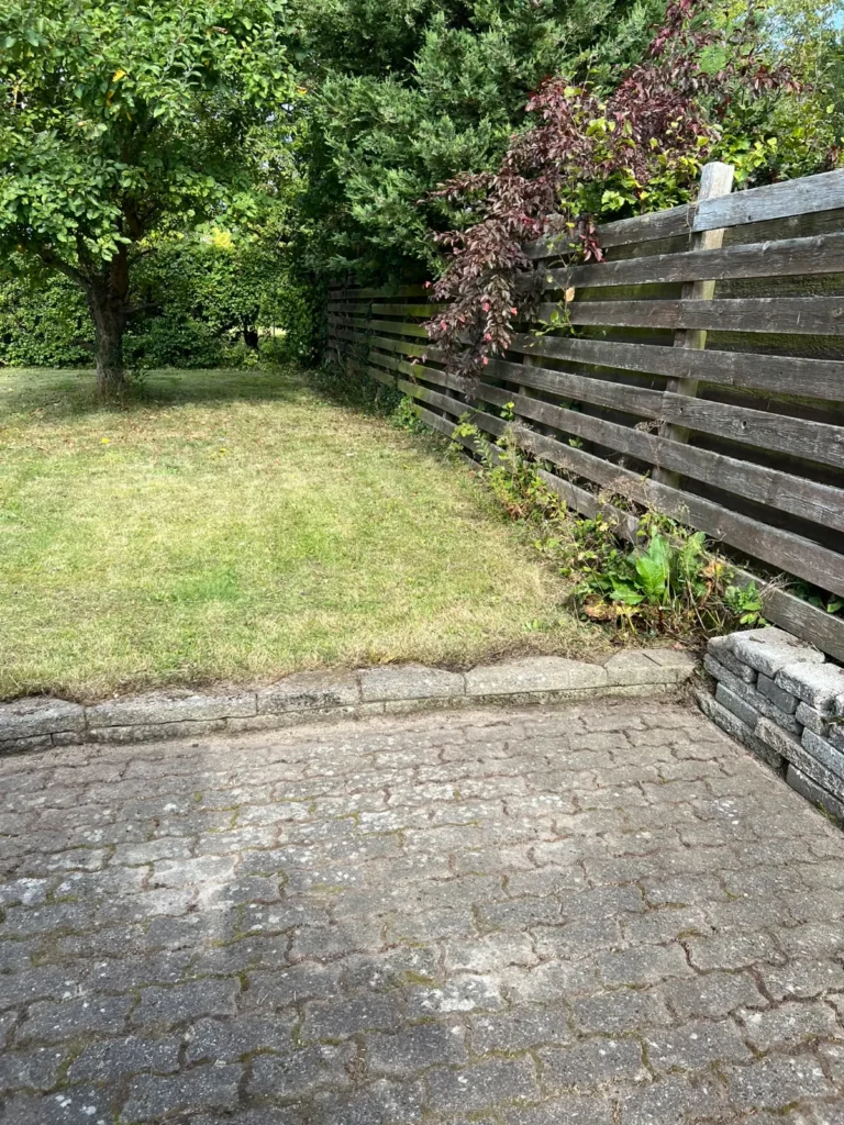 Have med græsplæne og flisebelægning langs plankeværk